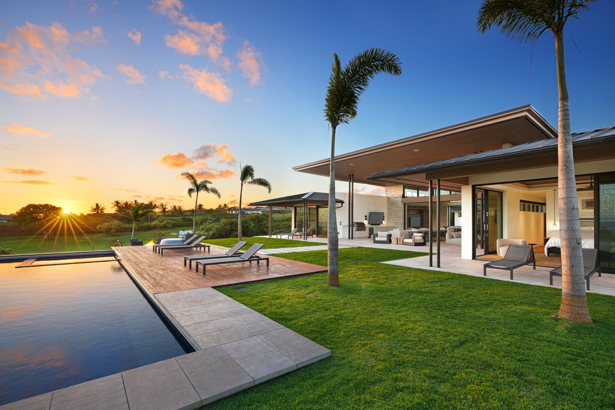 A pool and patio area with grass, palm trees, and a sunset.