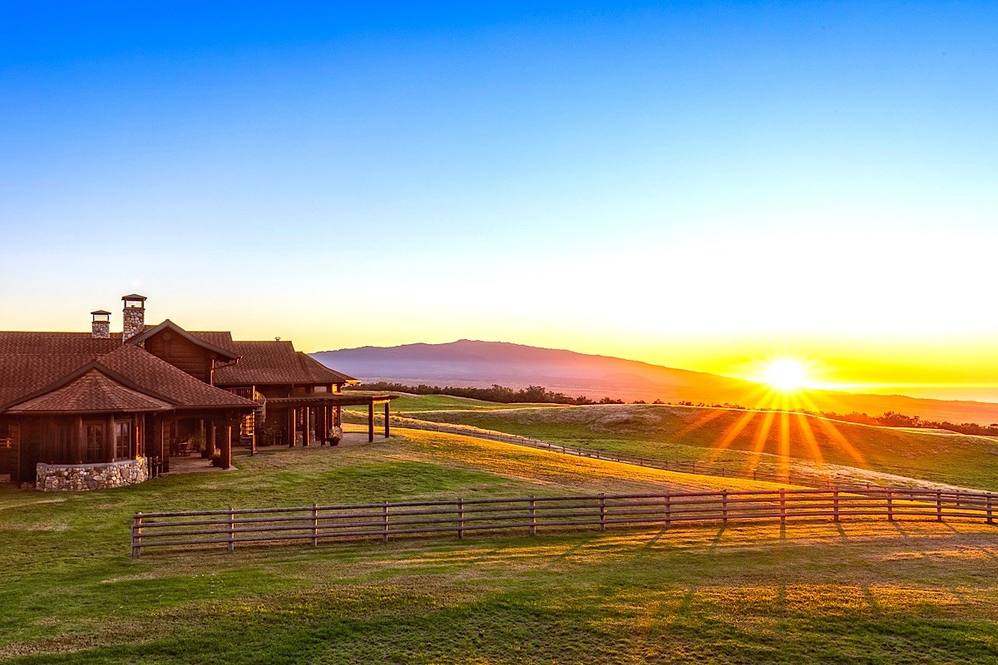 A sunset over a farm house and field.