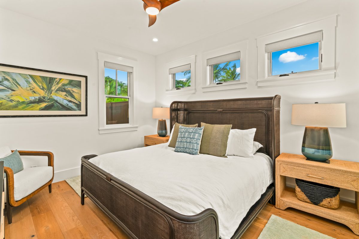 A bedroom with a bed, two nightstands and three windows.